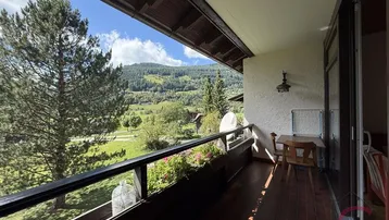 Geräumiger Balkon mit Holzboden, Sitzgelegenheiten und weitem Blick auf die umliegende Berglandschaft.
