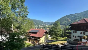 Gebäude in alpiner Landschaft mit Bergblick, umgeben von viel Grün und klarem Himmel. Ein Haus verfügt über Solarpaneele auf dem Dach.