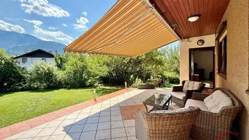 Gemütliche Terrasse mit Korbmöbeln, ausziehbarer Markise und weitem Blick auf Berge und Garten.