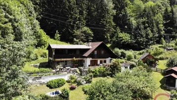 Haus in Hanglage umgeben von Wald und Grünflächen mit Terrassenbereichen und Bergblick.