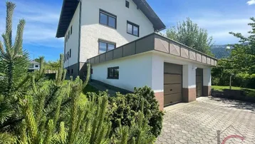 Einfamilienhaus mit Doppelgarage und gepflasterter Auffahrt, umgeben von grüner Landschaft.