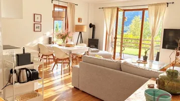 Heller offener Wohn-Essbereich mit Holzboden, Kaminofen und Zugang zur Terrasse mit Bergblick.
