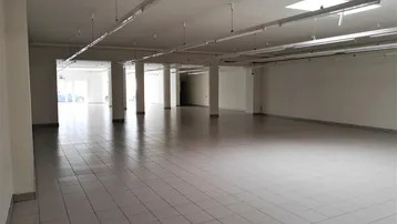 Geräumiger, leerer Gewerberaum mit Fliesenboden, hohen Decken und Säulen, ideal für Einzelhandel.