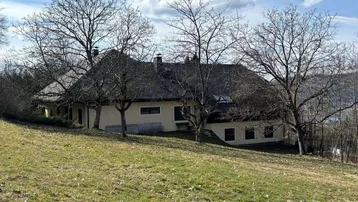 Landhaus auf einem Hügel mit weitem Blick und umgeben von kahlen Bäumen im Frühling.