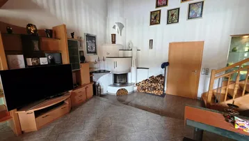 Gemütliches Wohnzimmer mit einem markanten Kaminofen, Holzscheiten und einem TV-Möbel. Der Raum wirkt hell und einladend.