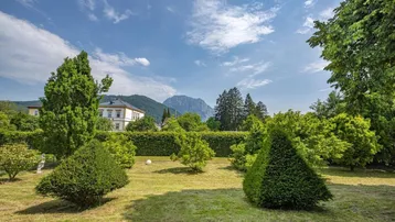 Gepflegter Garten mit Rasenflächen, Bäumen und einem malerischen Bergblick im Hintergrund.