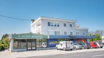 Gebäude mit Bäckerei und Casino im Erdgeschoss sowie Wohnungen in den oberen Stockwerken unter blauem Himmel.