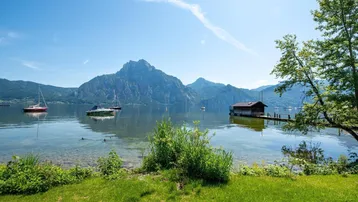 Malerischer Blick auf den See mit majestätischen Bergen im Hintergrund und einem kleinen Bootshaus am Ufer.