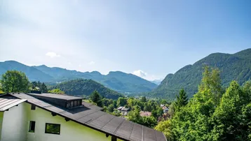 Panoramablick auf die umliegende Berglandschaft mit einem Teil des Gebäudedachs im Vordergrund.