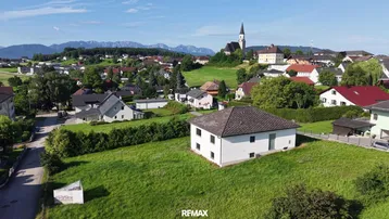 Luftaufnahme eines Einfamilienhauses in ländlicher Umgebung mit Bergblick und Kirchturm.