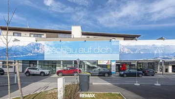 Modernes Gebäude mit großer Werbeplane und darüberliegenden Wohneinheiten unter blauem Himmel.