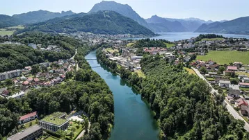 Luftaufnahme einer Stadt am Fluss mit See- und Bergblick in der Ferne.