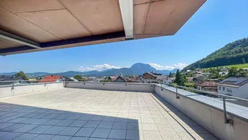 Geräumige Dachterrasse mit Fliesenboden, Markise und weitem Blick auf die umliegende Berglandschaft.