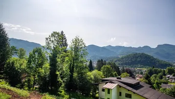 Panoramablick auf ein Haus in grüner Hanglage mit weitreichender Berglandschaft im Hintergrund.