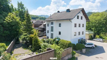 Großes Wohnhaus mit weißer Fassade, umgeben von viel Grün und Bäumen in ländlicher Umgebung.