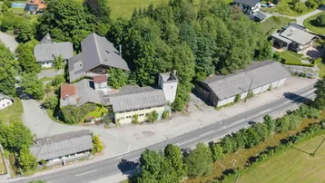 Luftaufnahme des Anwesens mit mehreren Gebäuden, umgeben von viel Grün und einer Straße.