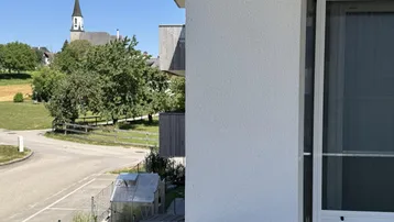 Blick von einem Balkon auf die Umgebung mit Kirche, Straße und Grünflächen.