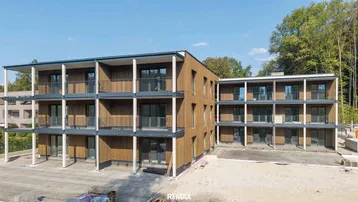 Modernes Mehrfamilienhaus mit Holzfassade und mehreren Balkonen, umgeben von viel Grün.