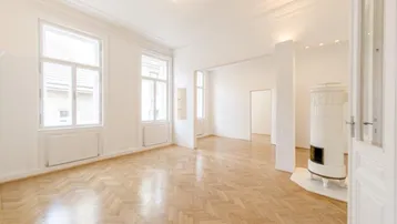 Helles Wohnzimmer mit Fischgrätparkett, hohen Decken und einem traditionellen Kachelofen.