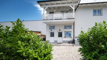 Vorderansicht des modernen Hauses mit weißer Fassade, Eingangsbereich und einem Balkon im Obergeschoss.