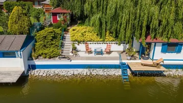 Vogelperspektive eines idyllischen Grundstücks am Wasser mit Terrasse, Gartenmöbeln und direktem Seezugang.