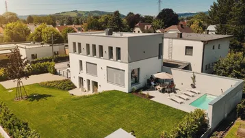 Modernes Haus mit großem Garten, Terrasse und kleinem Pool, umgeben von grüner Landschaft.