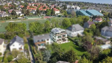 Luftaufnahme eines modernen Hauses mit Solaranlagen auf dem Dach und großem Garten in grüner Umgebung.