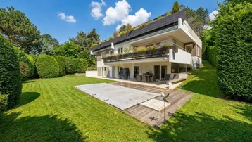 Großzügiger Gartenbereich mit Rasenfläche, Poolabdeckung und einer Holzterrasse vor dem Haus.