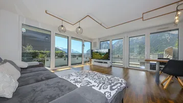 Helles Wohn- und Esszimmer mit Holzboden, großen Fenstern und beeindruckendem Bergblick.