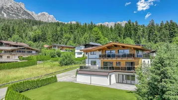 Modernes Haus in den Bergen mit Holzelementen, großen Balkonen und gepflegtem Garten.