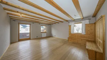 Geräumiges Wohnzimmer mit Holzbalkendecke, hellem Holzboden und Zugang zum Balkon.