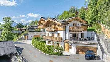 Luxuriöse alpine Villa mit Holzfassade, Balkonen und gepflegter Auffahrt in sonniger Lage.