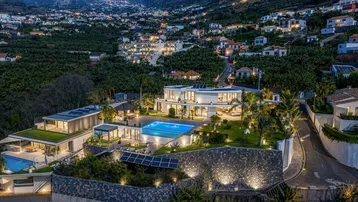 Luxuriöse Villa bei Nacht, umgeben von beleuchteten Gärten und Bananenplantagen mit Blick auf die Stadt.