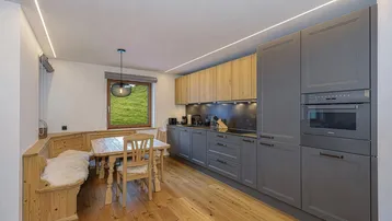 Moderne Küche mit grauen und holzfarbenen Schränken, Essbereich und Blick ins Grüne.