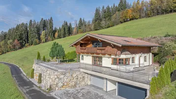 Charmantes Chalet mit Holzfassade, Steinsockel und integrierter Garage in idyllischer Hanglage.