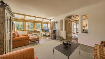 Helles Wohnzimmer mit Holzofen, traditionellen Möbeln und großen Fenstern mit Bergblick.
