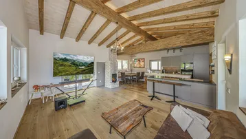 Offener Wohn-Essbereich mit Holzbalkendecke, Kamin und moderner Küche in den Bergen.
