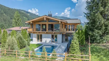 Modernes Chalet mit Holzfassade, großem Garten und privatem Pool in alpiner Berglandschaft.