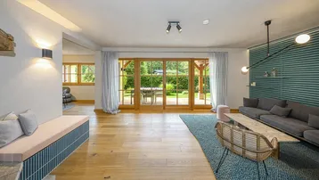 Geräumiges Wohnzimmer mit Holzboden und großen Fenstern, die den Blick ins Grüne freigeben.