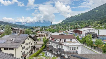 Weitläufiger Blick über eine Stadt in den Bergen mit vielen Häusern und grünen Hügeln.