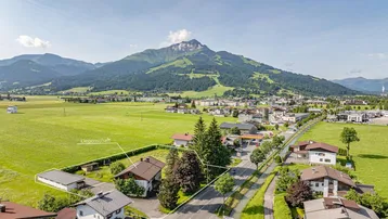 Luftaufnahme eines Grundstücks mit umliegenden Häusern, Feldern und Bergen im Hintergrund.