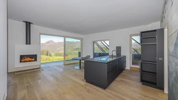 Offener Wohnbereich mit moderner schwarzer Küche, Kamin und Zugang zur Terrasse mit Panoramablick auf die Berge.