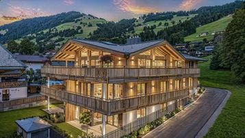 Modernes Holzhaus im alpinen Stil mit mehreren Balkonen und Bergblick bei Sonnenuntergang.
