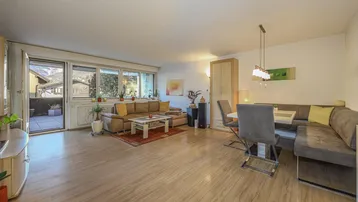 Heller Wohn-Essbereich mit Parkettboden, großzügigen Fenstern und Zugang zu einem Balkon.