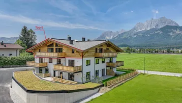Modernes Mehrfamilienhaus mit Holzfassade, Balkonen und beeindruckendem Bergblick.