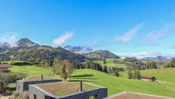 Panoramablick auf die grüne Hügellandschaft und die majestätischen Berge unter blauem Himmel.
