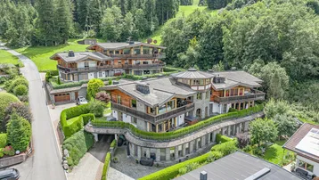 Luftaufnahme einer luxuriösen Wohnanlage im alpinen Stil, umgeben von grünen Wäldern und Bergen.