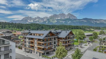 Moderne Wohnanlage mit Holzfassaden und Balkonen vor beeindruckender Bergkulisse.