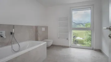 Modernes Badezimmer mit Badewanne, wandhängendem WC und Fenster mit Blick ins Grüne.