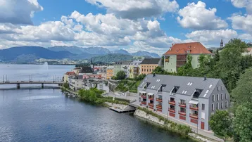 Panoramablick auf die Stadt am See mit Bergen im Hintergrund und dem modernen Gebäude am Ufer.